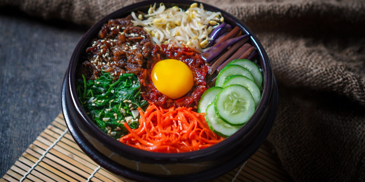 Seporsi bibimbap campur sayur dengan aneka warna sayuran segar, telur mata sapi, dan saus gochujang khas Korea