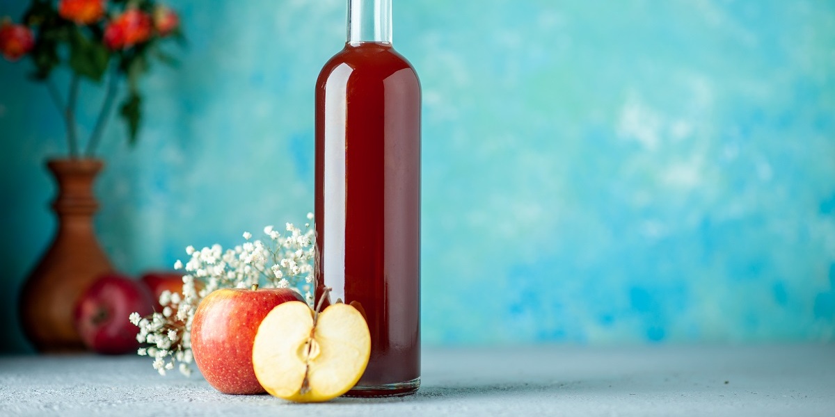 Botol cuka sari apel transparan dengan label organik diletakkan di atas meja kayu, dengan apel segar di sampingnya sebagai dekorasi